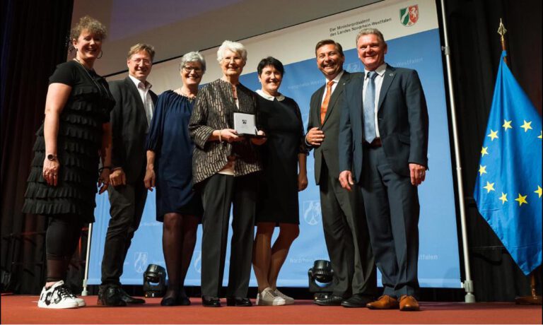 Margot Bollmann (M.) hat die Sportplakette des Landes NRW erhalten. Glückwünsche gab es im Beisein ihrer Familie von Andrea Milz (l.), NRW-Staatssekretärin für Sport und Ehrenamt, Stefan Klett (r.), Präsident des Landessportbundes NRW, sowie Daniel Wolski (2.v.r.), erster stellvertretender Bürgermeister der Stadt Lünen. Foto: Land NRW