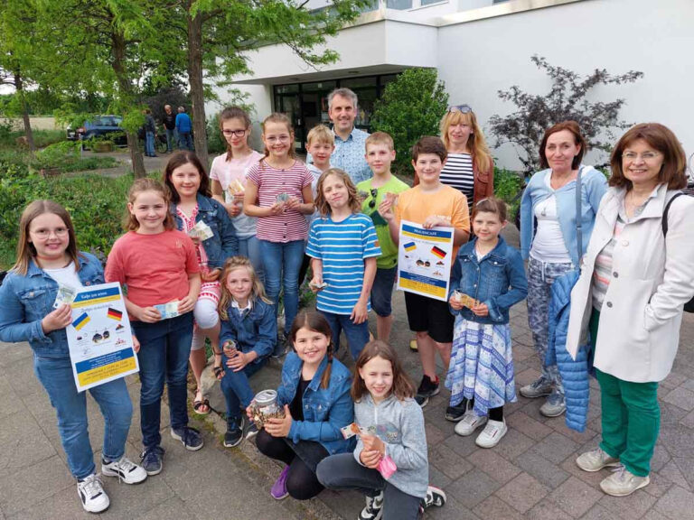 Lena Zimmermann, Leonard Zimmermann, Aaron Dankert, Pia Wenner, Marie Wenner, Sophia Marek, Lena Marek, Tom Neugebauer, Jasper Neugebauer, Jill Niehus, Ceyda Akkaya, Marlene Kroes und Fritz Wenner überreichten das Sparschwein an Pfarrer Alexander Meese und die Organisatorinnen des Frauen-Cafés. Foto: Wagner