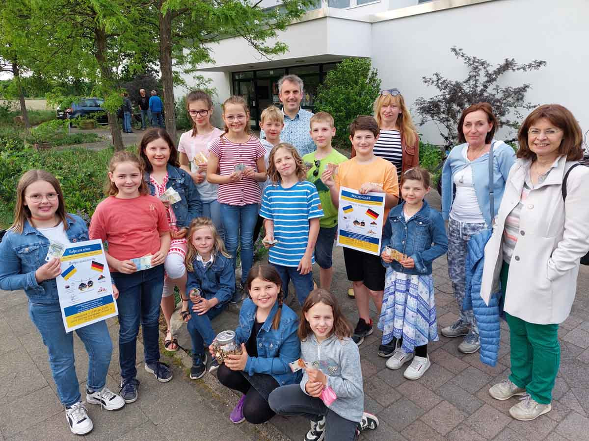 Lena Zimmermann, Leonard Zimmermann, Aaron Dankert, Pia Wenner, Marie Wenner, Sophia Marek, Lena Marek, Tom Neugebauer, Jasper Neugebauer, Jill Niehus, Ceyda Akkaya, Marlene Kroes und Fritz Wenner überreichten das Sparschwein an Pfarrer Alexander Meese und die Organisatorinnen des Frauen-Cafés. Foto: Wagner
