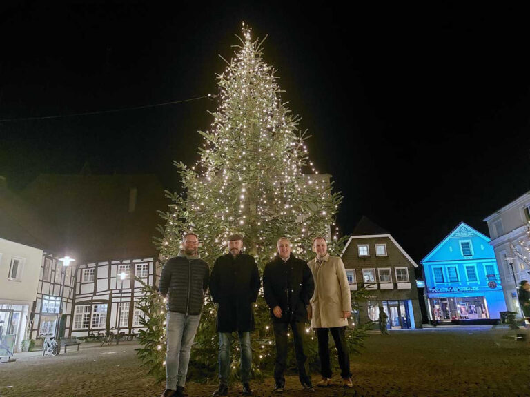 Unzählige Lichter bringen den Weihnachtsbaum auf dem Marktplatz zum Leuchten. Philipp Gärtner (von rechts), Markus Dyckhoff (beide Volksbank), Hubertus Waterhues und David Ruschenbaum freuen sich über das Ergebnis des gemeinsamen Projekts. Foto: Wagner