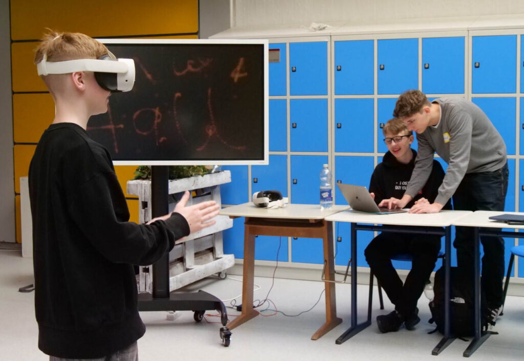 Ein Siebtklässler testet virtuelle Realität. Im Hintergrund: Zwei Schüler-Medienscouts des AFG, Fynn (links) und David (rechts). Foto: Schwarze