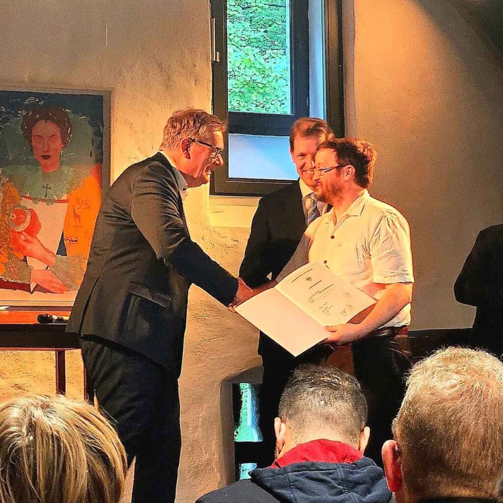 Mit der Einbürgerungsurkunde in der Hand nimmt Eric Eckmann die Glückwünsche von Bürgermeister Thomas Stohldreier entgegen. Im Hintergrund verfolgt Landrat Dr. Christian Schulze Pellengahr die feierliche Übergabe auf der Burg Vischering.